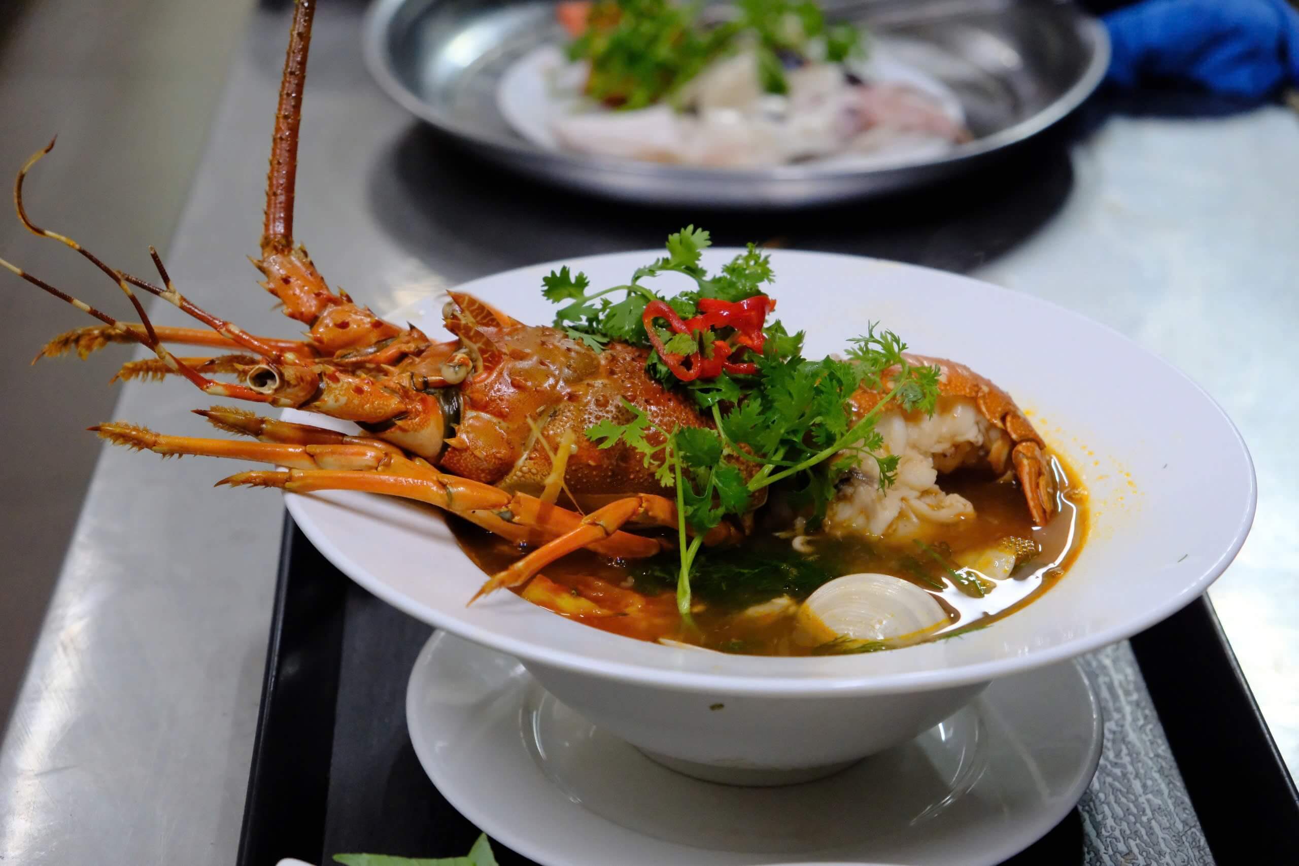 Các nguyên liệu sau khi chín được xếp ra tô. Tôm hùm được chia đôi phần đầu, phần bụng cũng được sơ chế để thực khách dễ cắt lấy thịt. Đầu bếp chan từ từ nước dùng đang sôi vào tô phở